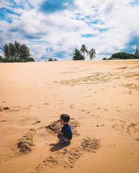 Kid sitting on sand at beach against sky