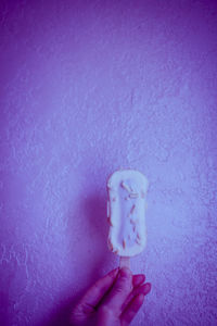 Close-up of person holding ice cream against wall