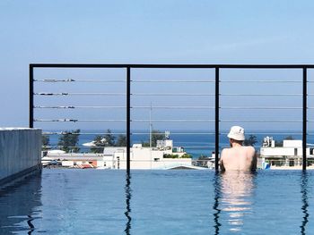 Rear view of shirtless man in swimming pool against clear sky