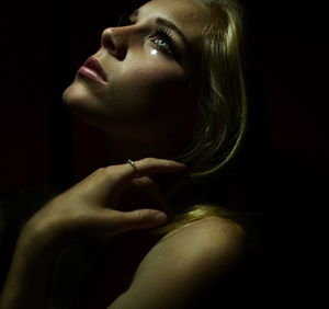 Close-up of sad young woman looking up against black background