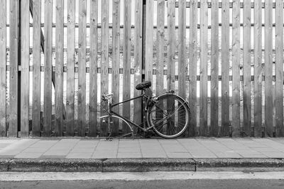 Damaged bicycle leaning on wooden fence