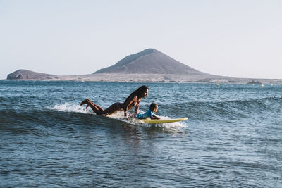 Pulled back view of mother and son surfing a small wave at sea