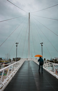 Rear view of people walking on suspension bridge against sky