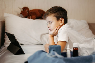 Little boy using tablet while laying in bed in living room. medicines in foreground out of focus