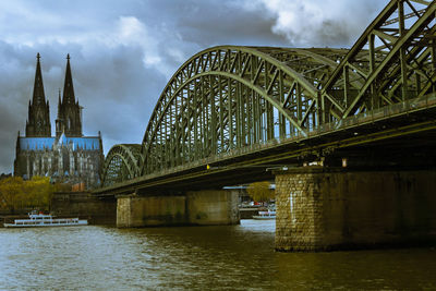 Low angle view of bridge over river against cloudy sky