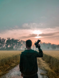 Rear view of man standing on field against sky during sunset