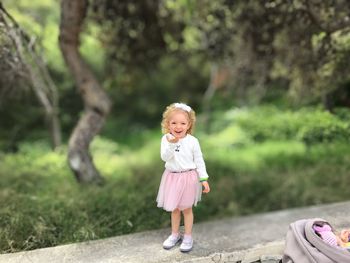 Portrait of smiling girl standing on retaining wall against tree