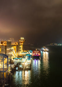 Illuminated city by sea against sky at night