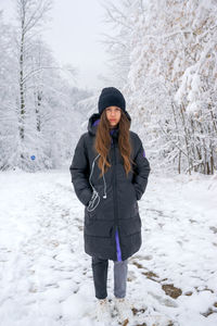 A girl in a black long warm jacket, in the middle of a snowy forest.