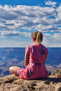 Rear view of woman sitting on cliff against sky