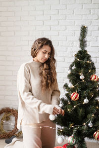 Young attractive woman decorating the christmas tree with fairy lights