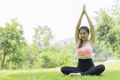 Full length portrait of woman practicing yoga while sitting on grassy field at park