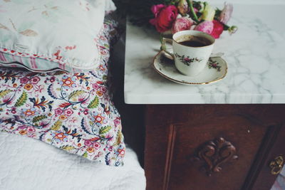 Close-up of coffee cup by flowers on table in bedroom