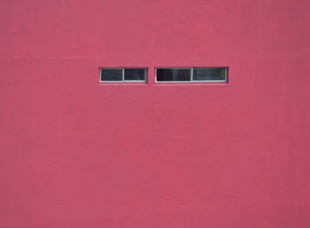 Close-up of rasperry-colored concrete wall and narrow windows