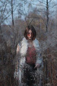 Young woman in hippie coat and red sunglasses among weeds and gr