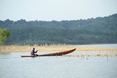 Side view of man in boat sailing on lake against sky