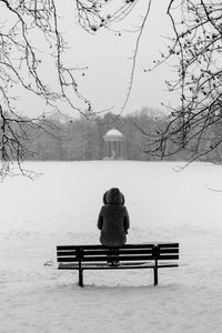 Rear view of woman sitting on bench in park during winter
