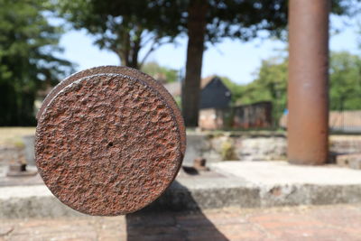 Close-up of circular rusty metal on stone against trees and sky.