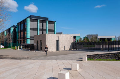 People walking on footpath by buildings against blue sky