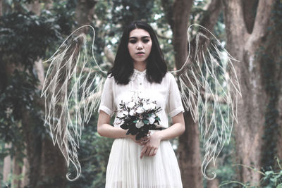 Digital composite image of woman with wings holding flowers in forest