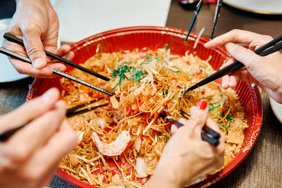A group of people celebrate chinese new year with a lohei or prosperity toss with chopsticks.