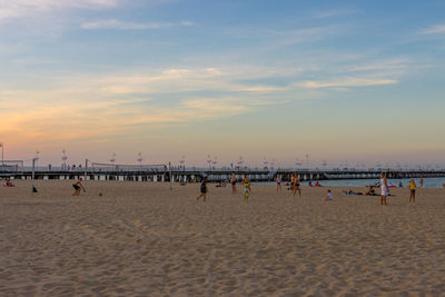 Group of people on beach against sky during sunset
