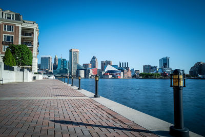 Footpath by river and buildings against blue sky