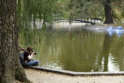 Side view of man sitting on lake in forest