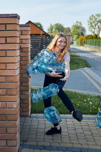 Full length of teenage girl falling plastic bottles while standing outdoors