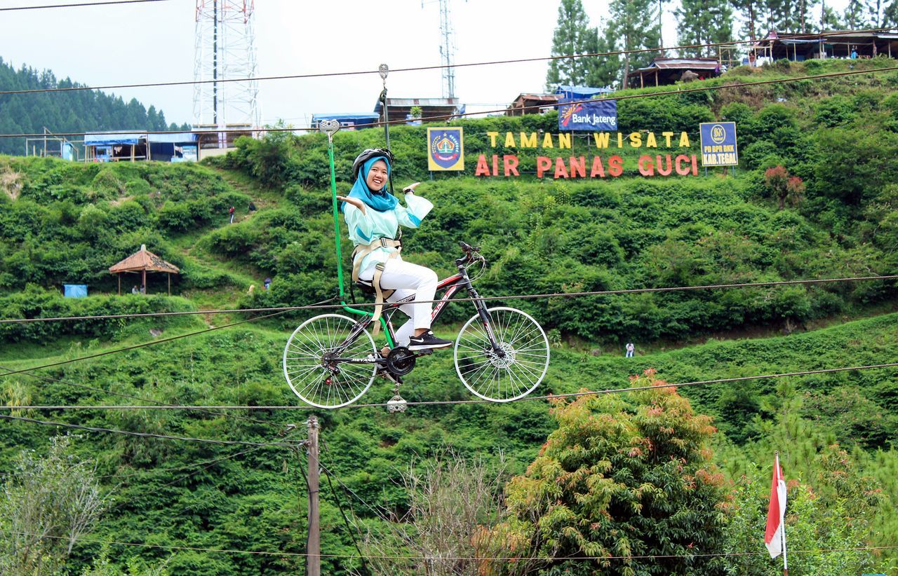 MAN RIDING BICYCLE ON FIELD BY TREES