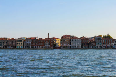 Buildings by sea against clear sky