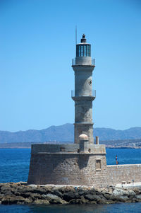 Lighthouse by sea against clear sky