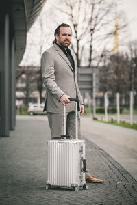 Portrait of businessman with suitcase standing outdoors