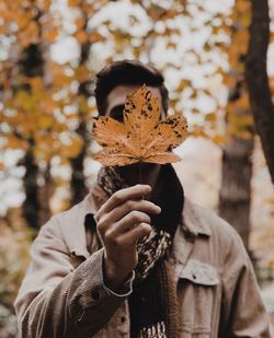Man holding maple leaf while standing in park during autumn