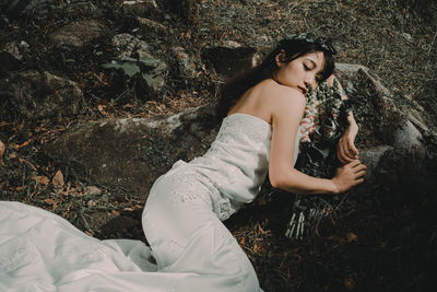 High angle view of woman with bouquet lying on field in forest