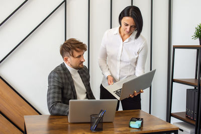 A man looks at a laptop to a woman in the office