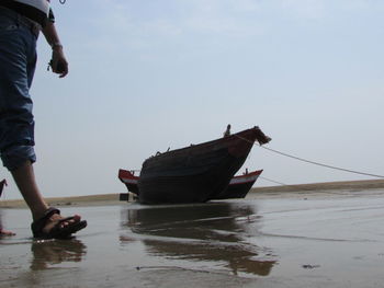 Low section of man standing on boat in sea against sky