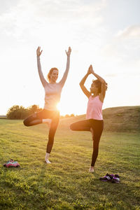 Happy mother and daughter practicing yoga on grass at park during sunset