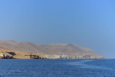 Scenic view of sea and mountains against clear blue sky