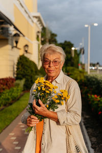 Portrait of smiling eldery women with yellow flowers  in orang dress