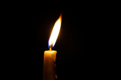 Close-up of burning candle against black background