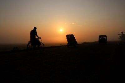 Silhouette man riding bicycle on street against sky during sun rise