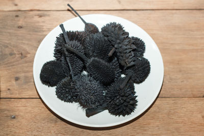 High angle view of black spiked plants in plate on wooden table