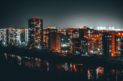 Illuminated buildings by river against sky at night