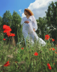 Rear view of pregnant woman standing by flowering plants on field