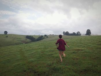 Full length of man standing on grassy field against cloudy sky