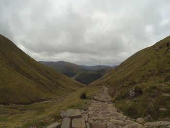 Scenic view of path in valley against cloudy sky