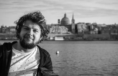 Portrait of smiling young man against river in city