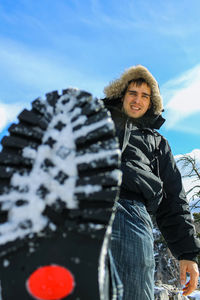 A close-up of the sole of the boot in the snow. in the background is a young man in a black jacket