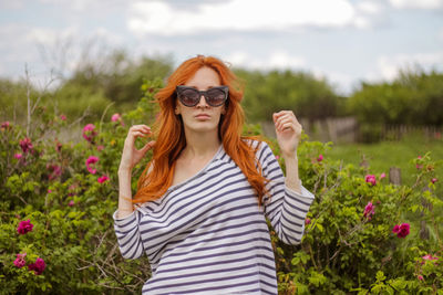 Beautiful young woman near rose bush